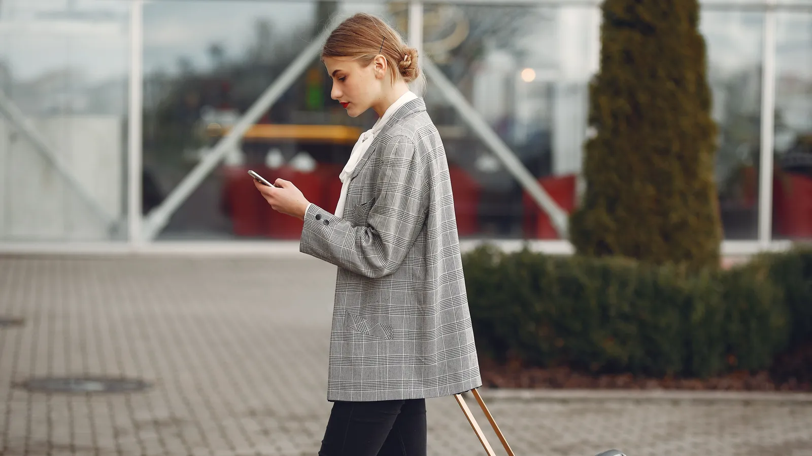 Traveller checking her phone outside an airport terminal, suitcase in hand
